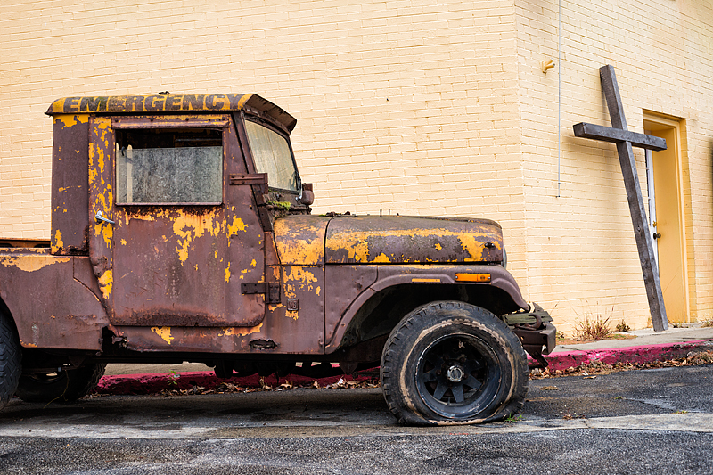 Rusted jeep with a flat tire sits outside the Capitol Restoration shop where a wooden cross leans against the door. The salvage shop serves at the Triple Crown Cowboy church on Thursday nights and Sunday mornings in Frankfort, Kentucky, USA.