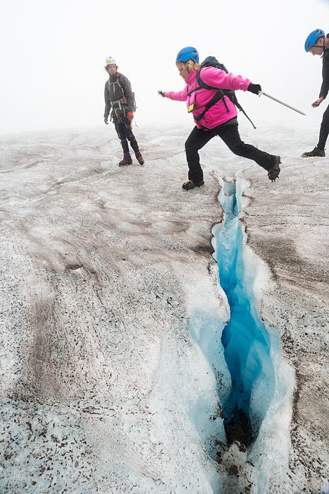 Woman jumps over a crevasse on Lemon Glacier, Juneau Icefield, Juneau, Alaska, USA