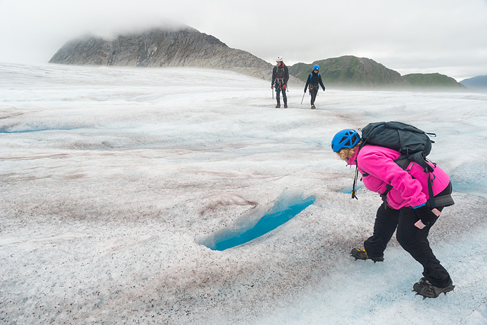 Woman looks into a crevasse with blue ice during a trekking adventure on Lemon Glacier, Juneau Icefield, Juneau, Alaska, USA