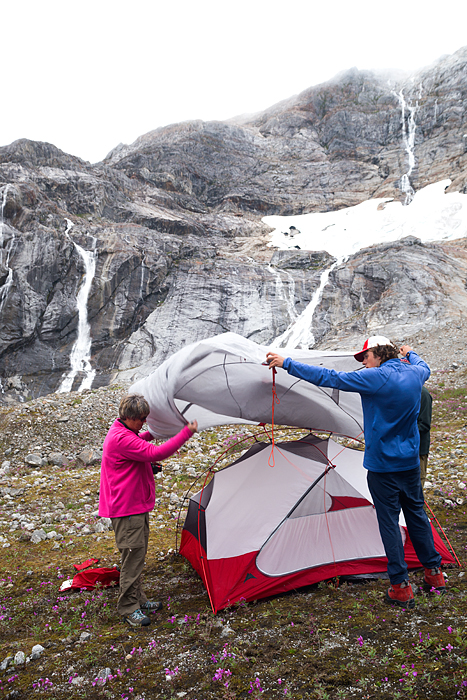 Senior woman and male guide in 20s set up tent for overnight camp, Lemon Glacier, Juneau, Alaska