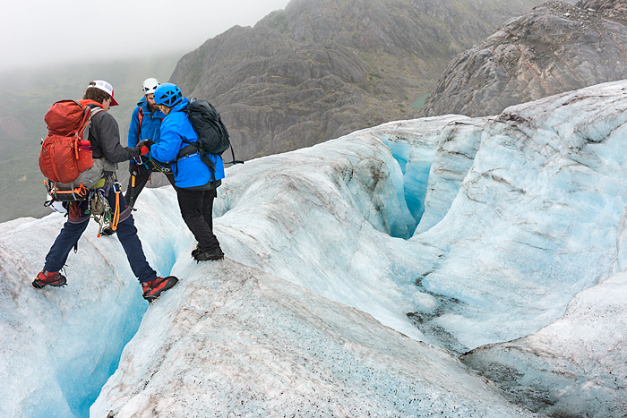 guides help woman across crevasse on glacier, Campsite of tent in glacier valley with mineral lake and waterfall at Lemon Glacier, Juneau Icefield, Juneau, Alaska, USA