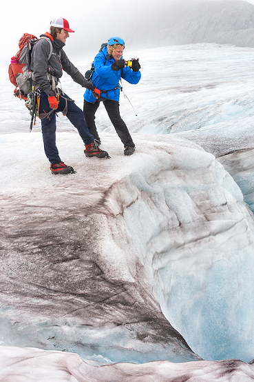 guide holds harness on woman looking into crevasse