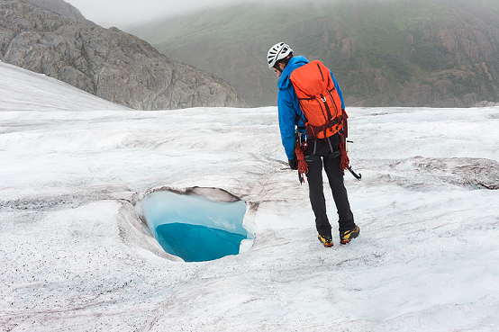 man looks into moulin on glacier, Campsite of tent in glacier valley with mineral lake and waterfall at Lemon Glacier, Juneau Icefield, Juneau, Alaska, USA