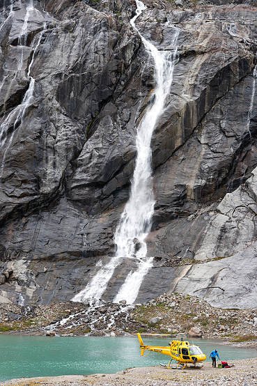 Helicopter lands beside green mineral lake and waterfall on Lemon Glacier, Juneau Icefield, 