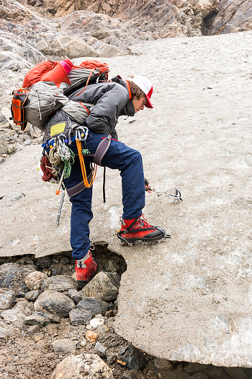 man puts on boot crampons for glacier hike