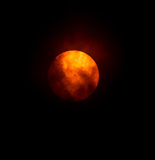 sun in full disc with swirling clouds after eclipse over