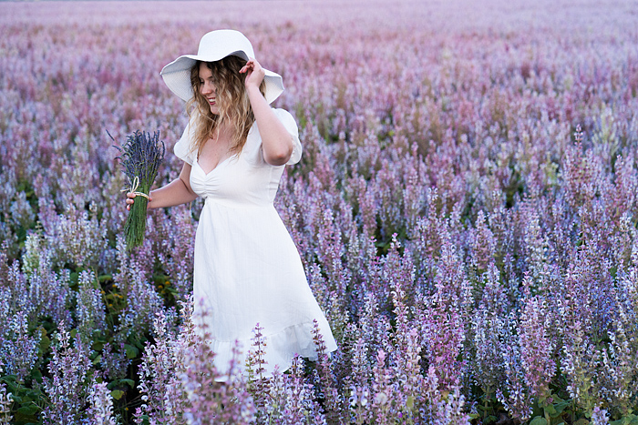 Clary sage, Pretty blond woman in a white dress walks through a blooming field, Valensole, Provence, France